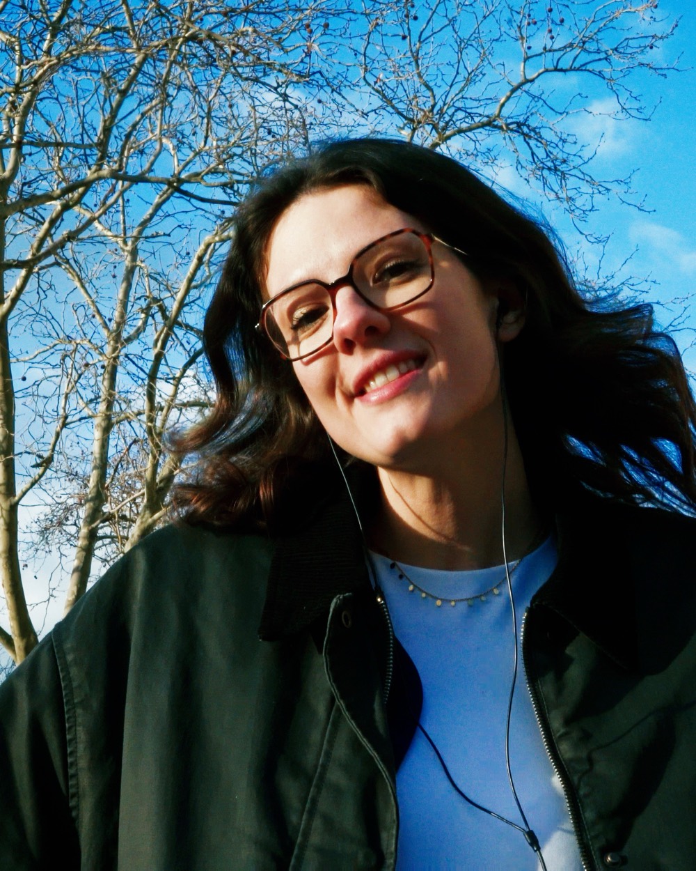 Portrait souriant d'une femme à lunettes, ciel bleu et arbres